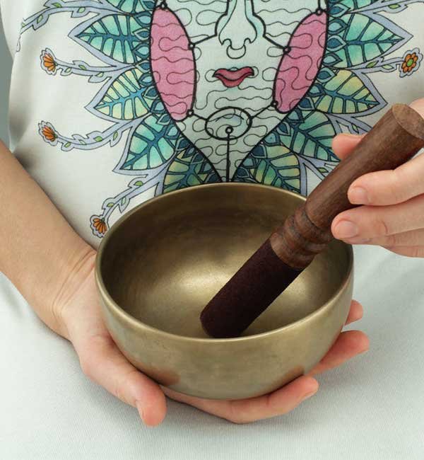 Hands holding a Tibetan singing bowl and wooden striker