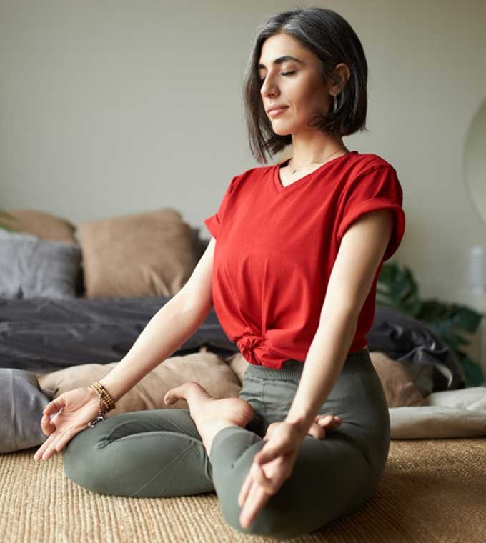 Woman meditating cross-legged at home with eyes closed and hands resting on her knees
