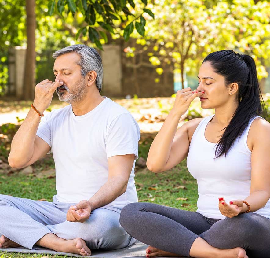 A man and a woman seated outdoors practising alternate-nostril breathing